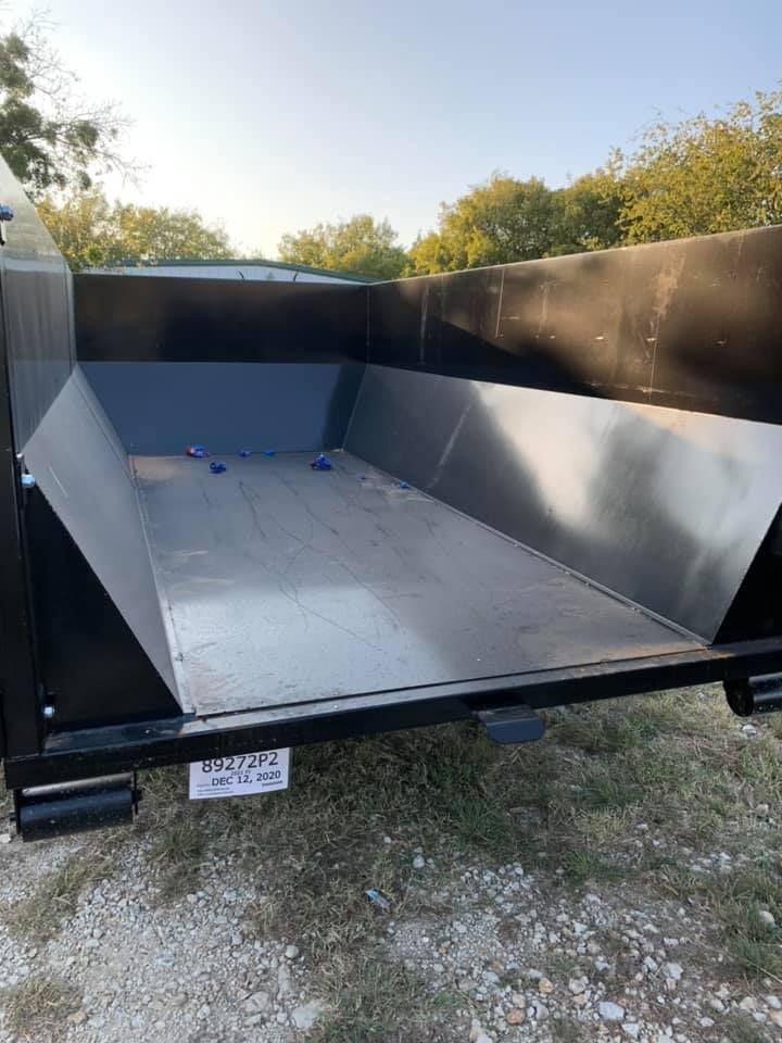 A dumpster is sitting on top of a gravel road.