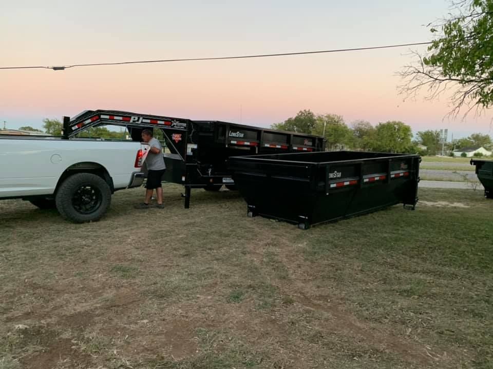 A man is standing next to a dumpster and a truck.