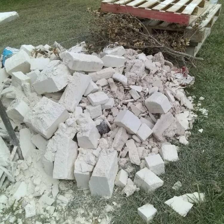 A pile of bricks sits in the grass next to a wooden pallet