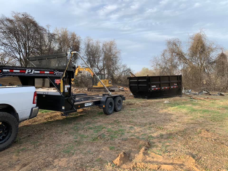 A dumpster is being towed by a truck in a field.
