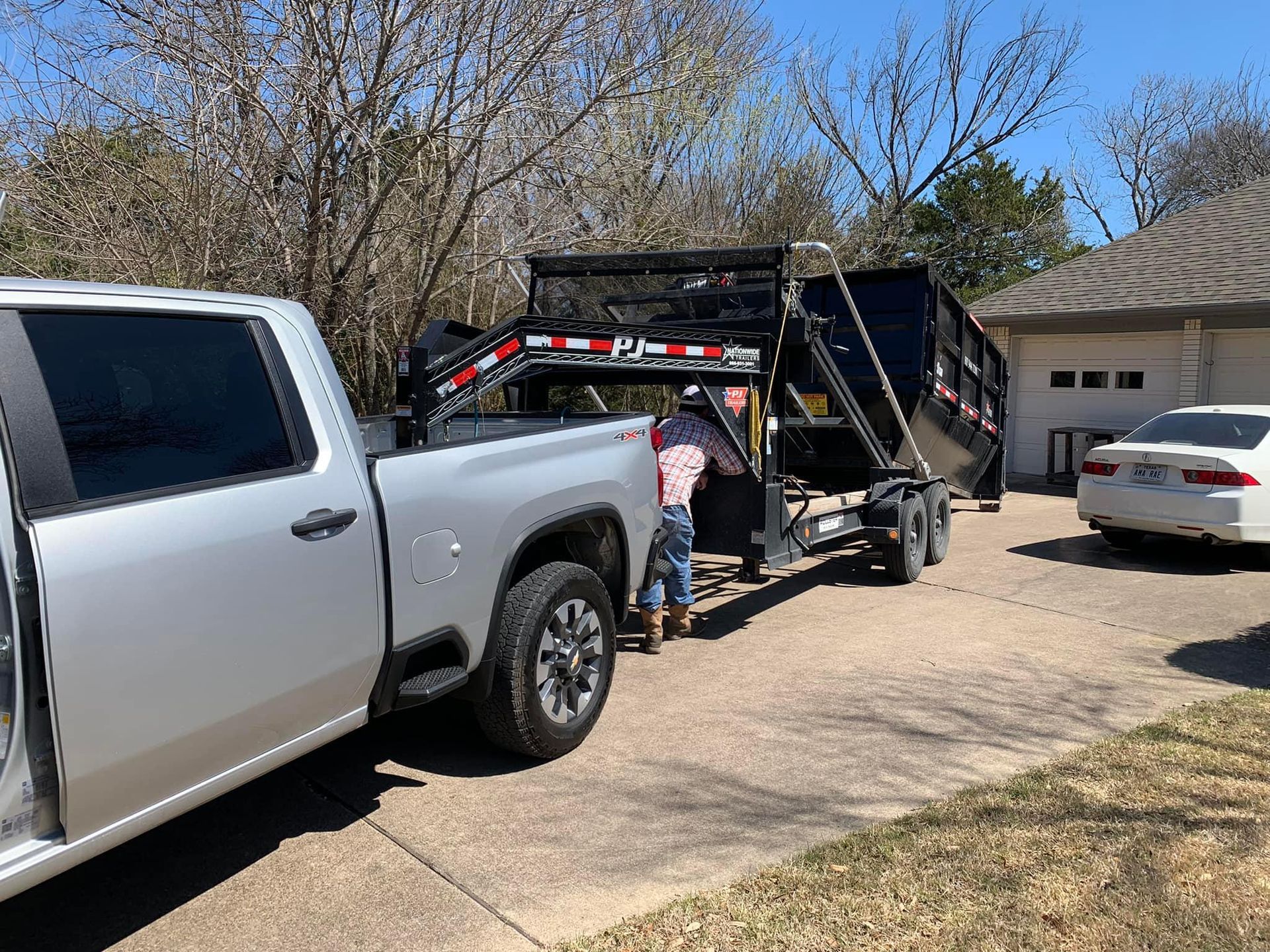 A truck is pulling a dumpster trailer in a driveway.