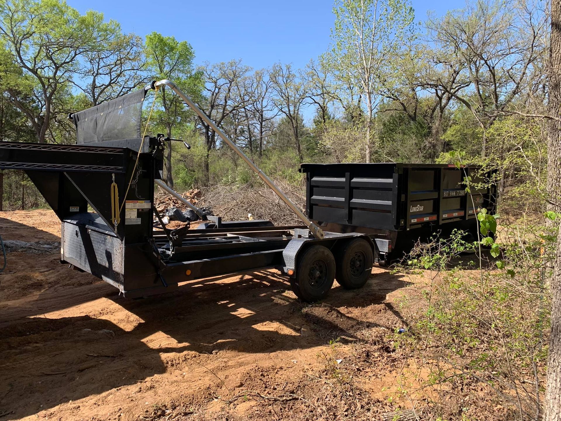 A dump trailer is parked next to a dumpster in a dirt field.