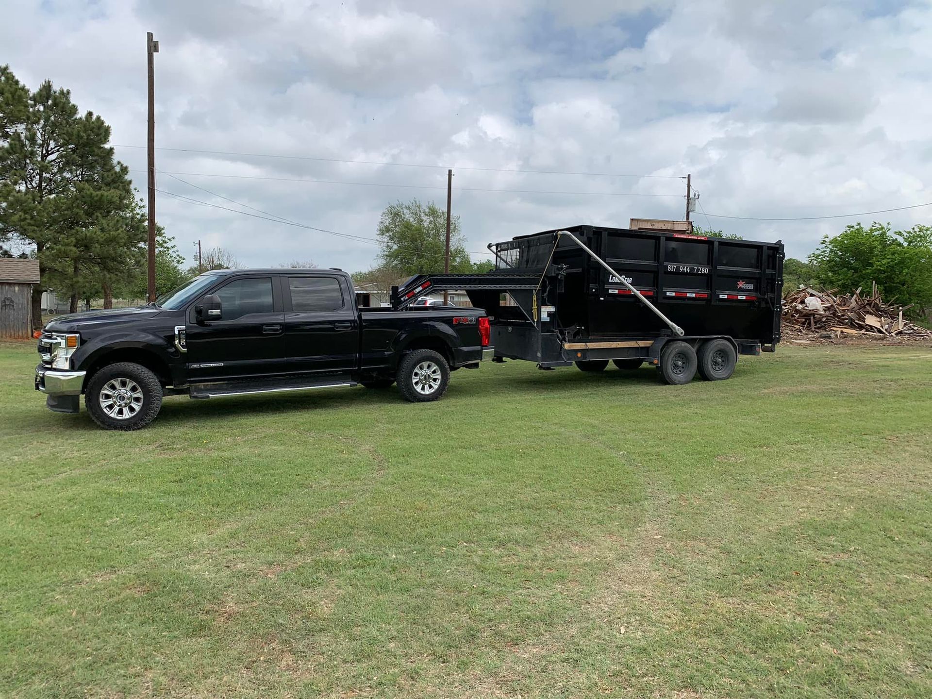 A black truck is towing a dumpster on a trailer.