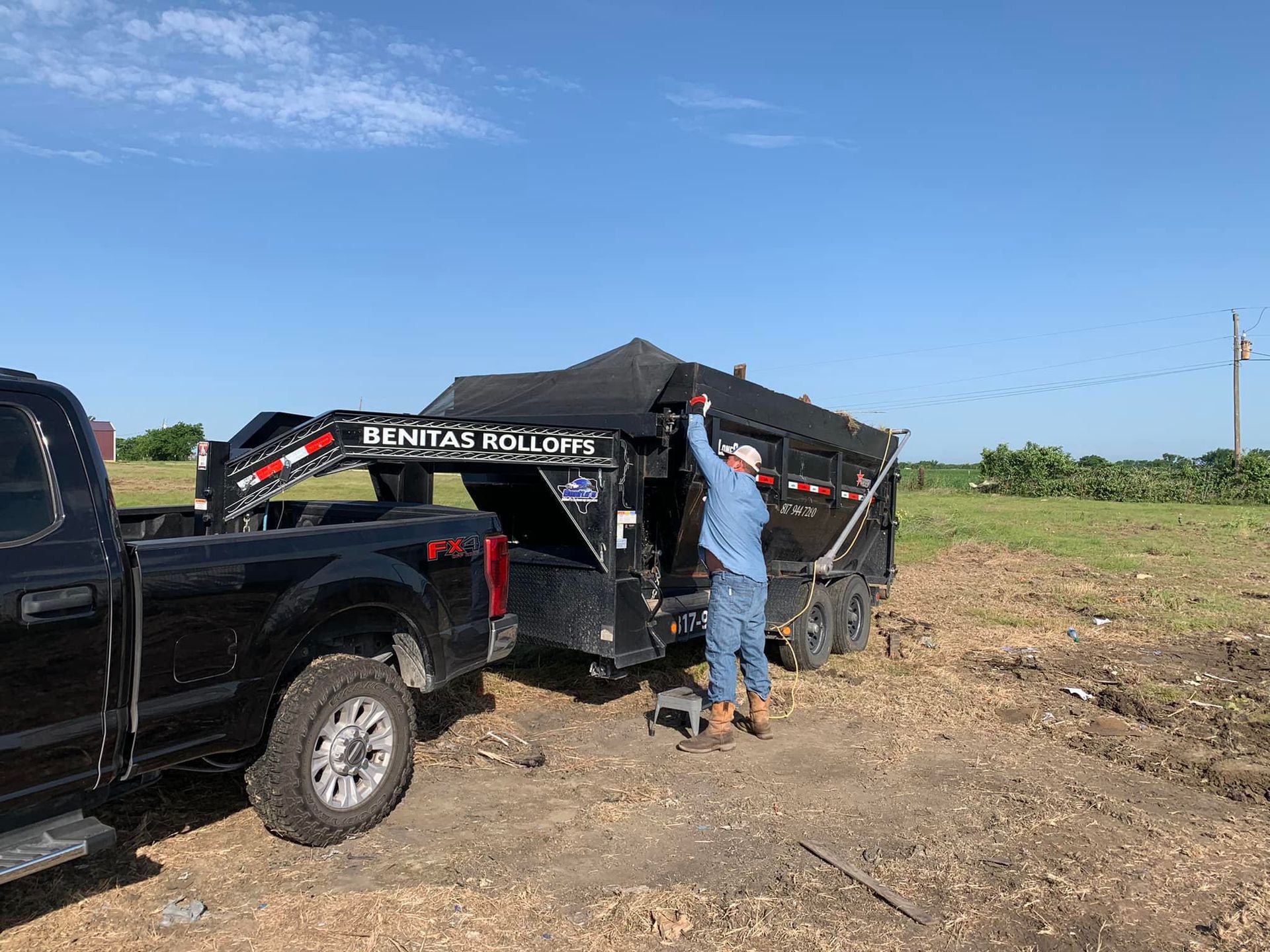 A man is loading a trailer into a truck in a field.