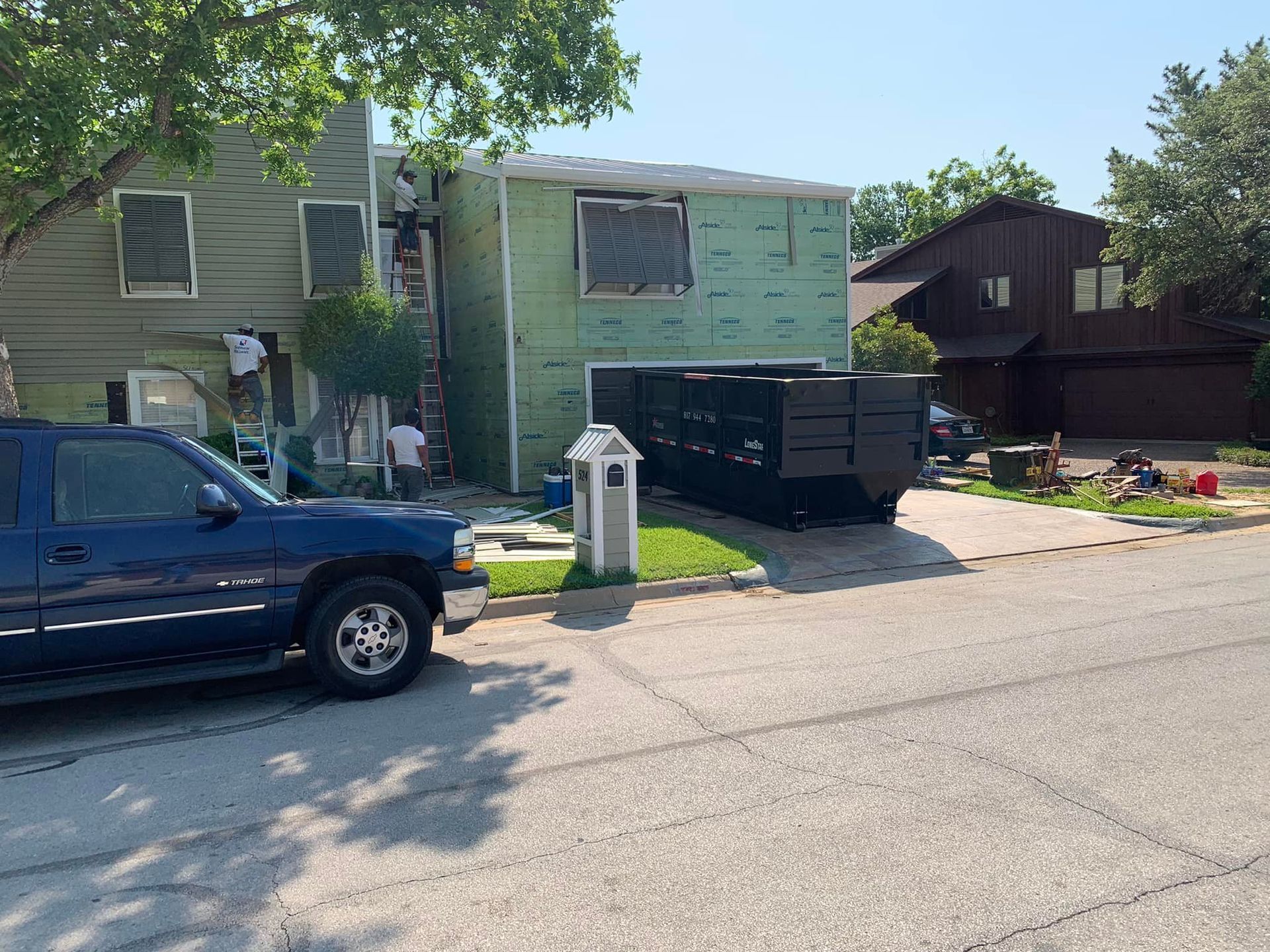 A blue truck is parked in front of a house being painted.