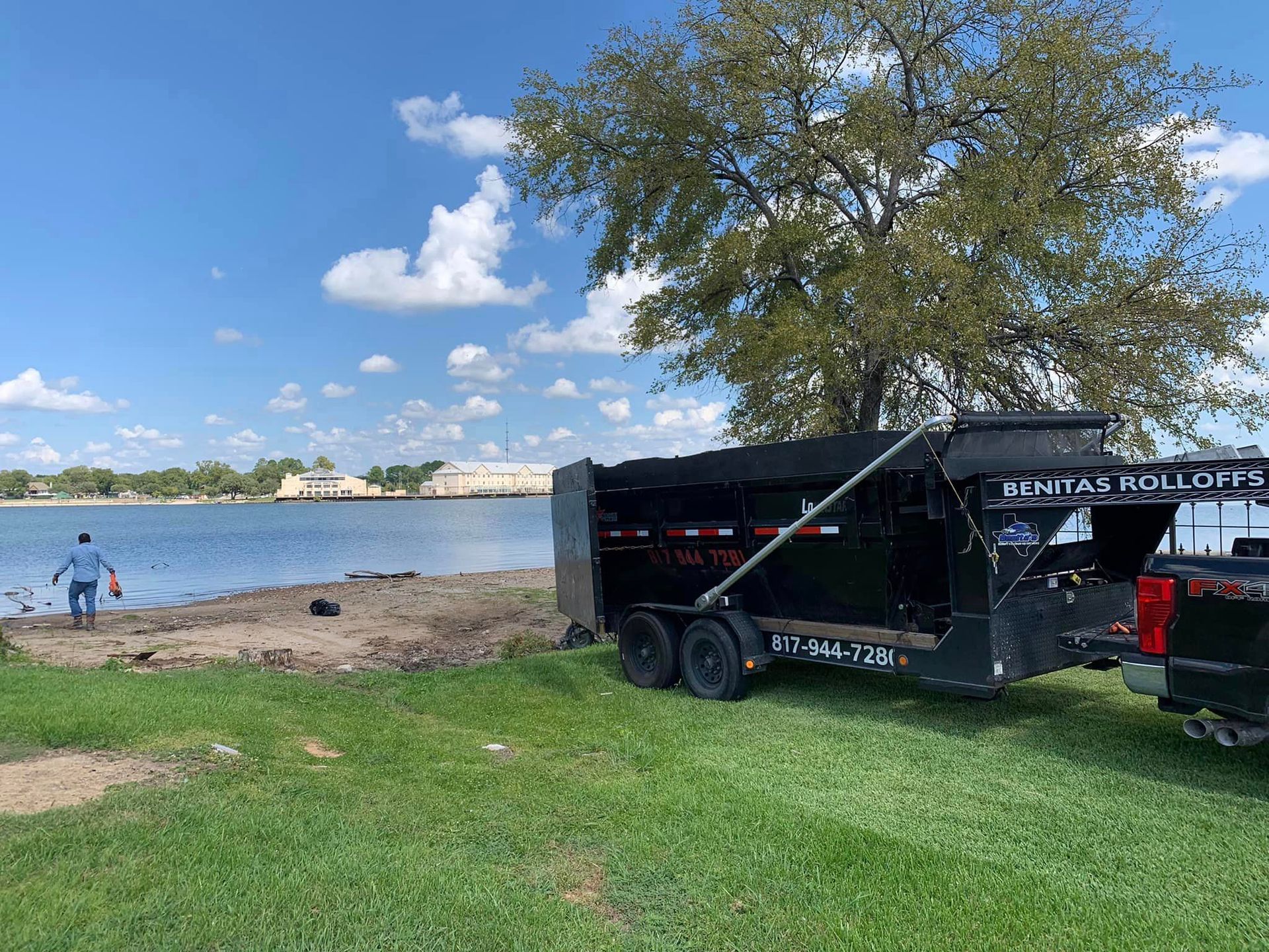 A dump truck is parked on the grass next to a lake.