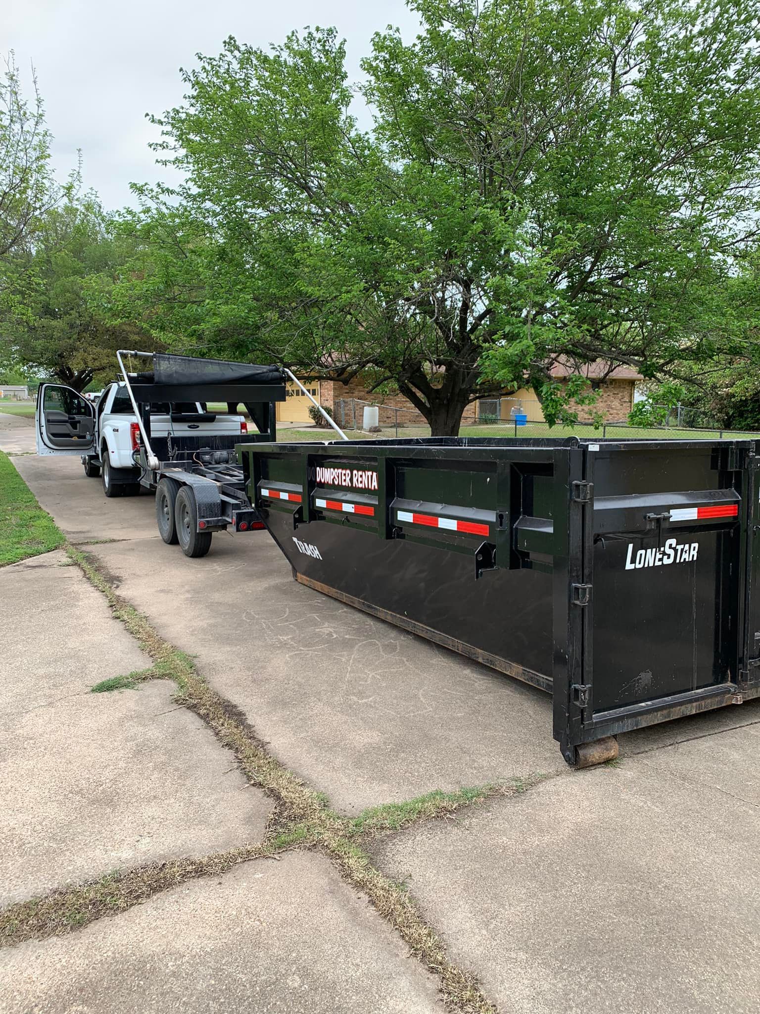 A dumpster is being towed by a truck in a driveway.