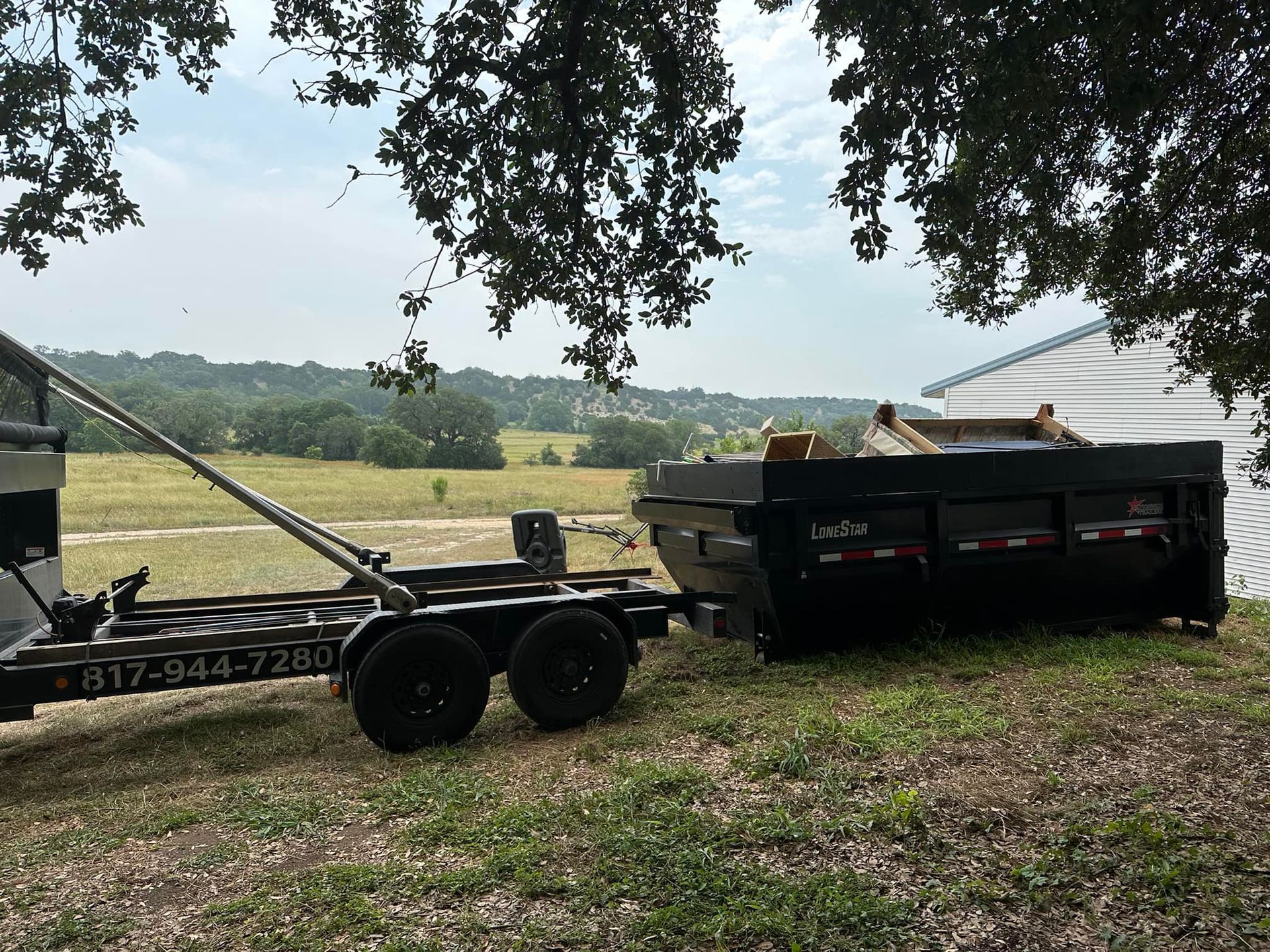 A dumpster is being pulled by a trailer in a field.
