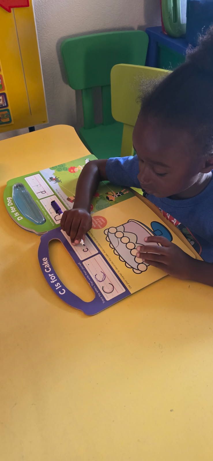 Child reading a book at a yellow table; book displays 