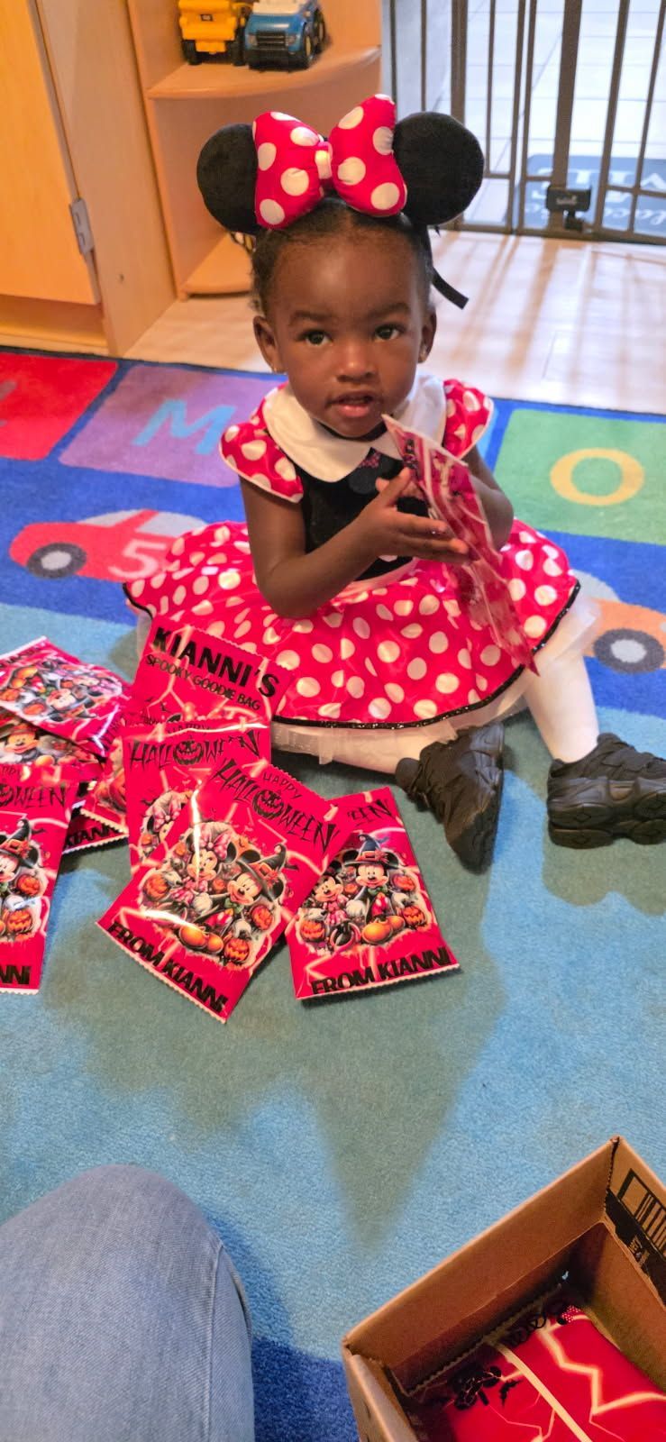 A child in a Minnie Mouse costume sits surrounded by snacks on a colorful rug.