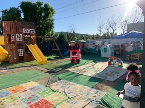 Playground with wooden structures, slides, and a child with a pink bow.