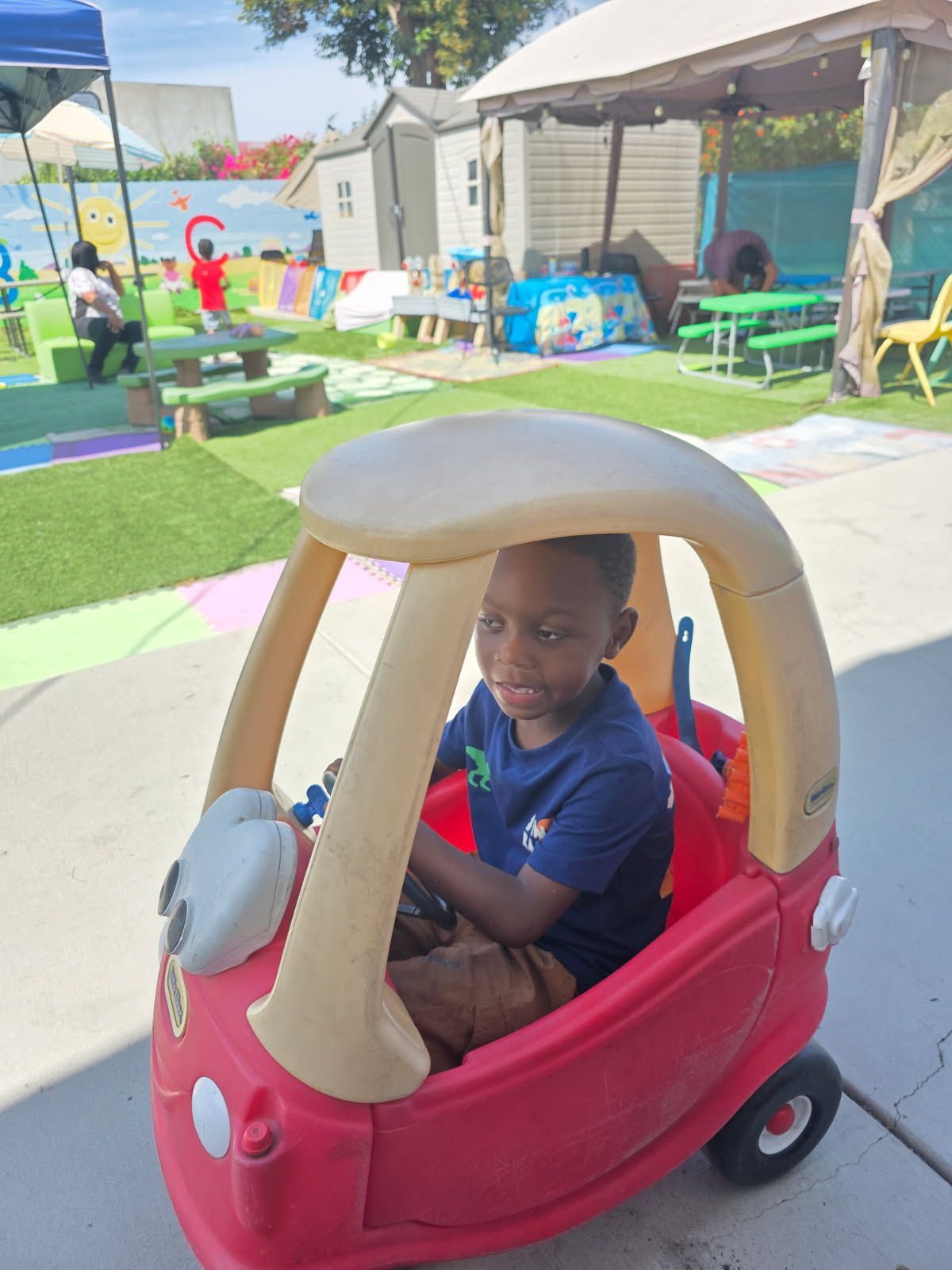 Boy sitting in a red and tan toy car outdoors.