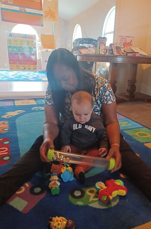 Woman and baby on a colorful mat playing with toys in a room.