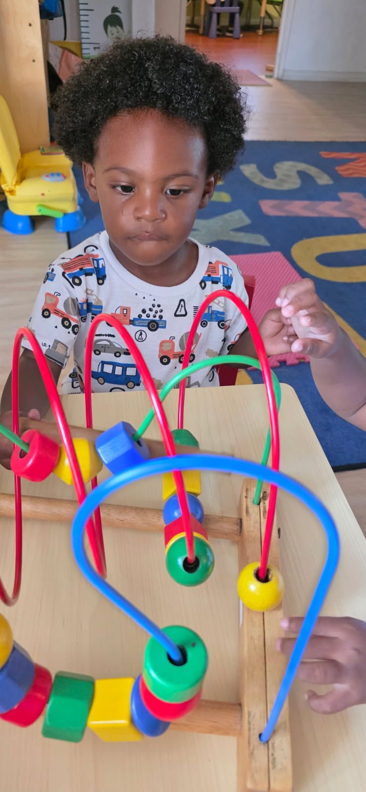 Child playing with a bead maze, focused expression. Colorful beads on wooden frame, indoors.