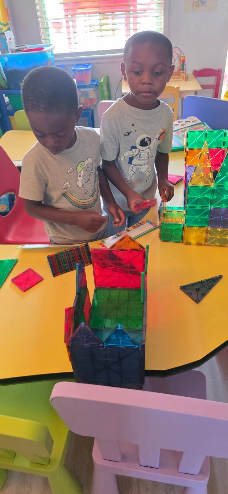 Two children building a structure with colorful magnetic blocks at a table in a classroom.