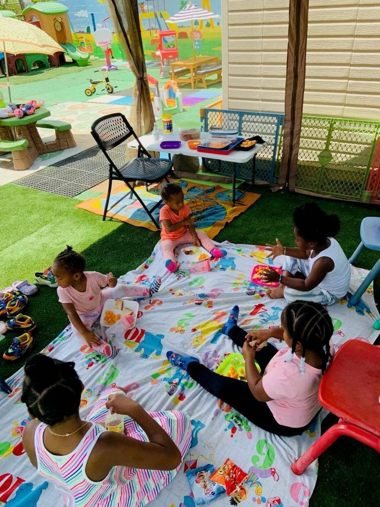 Children playing on a blanket outdoors; toys and a folding chair are nearby.