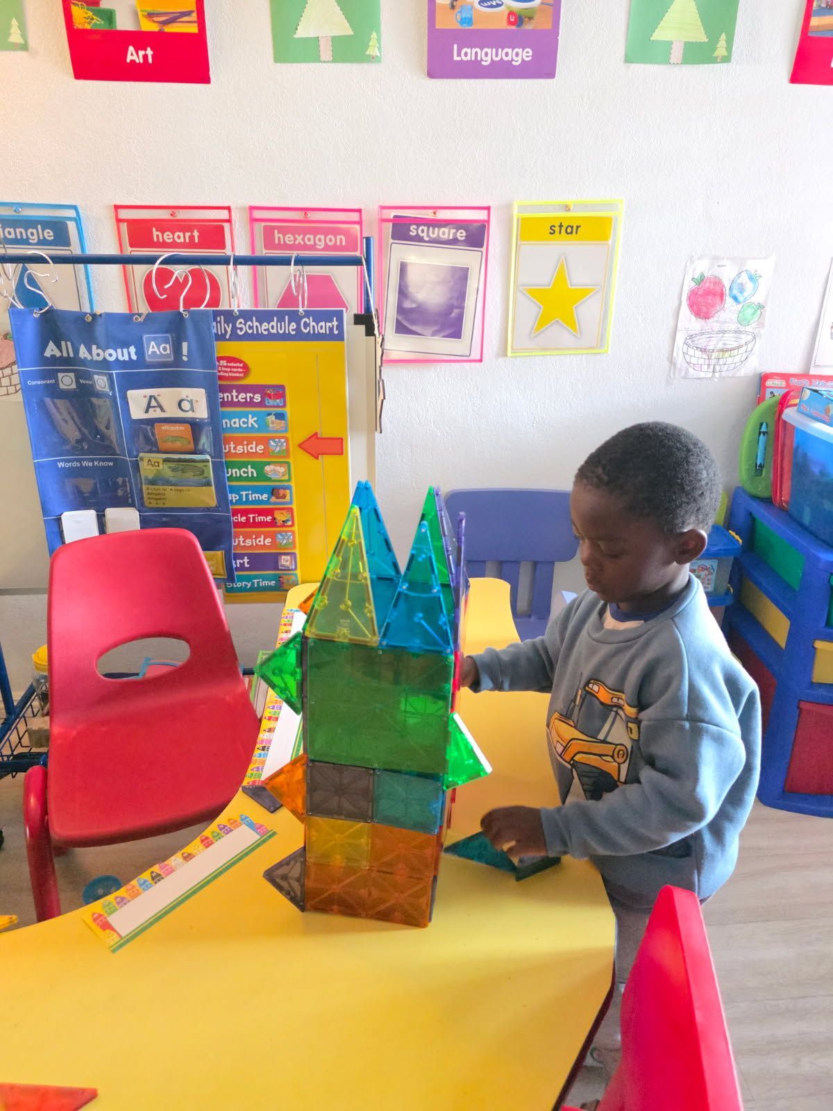 A child building with colorful magnetic tiles at a table in a classroom.