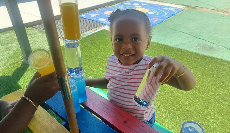 Child playing with colorful water tubes and a glass of juice outdoors.
