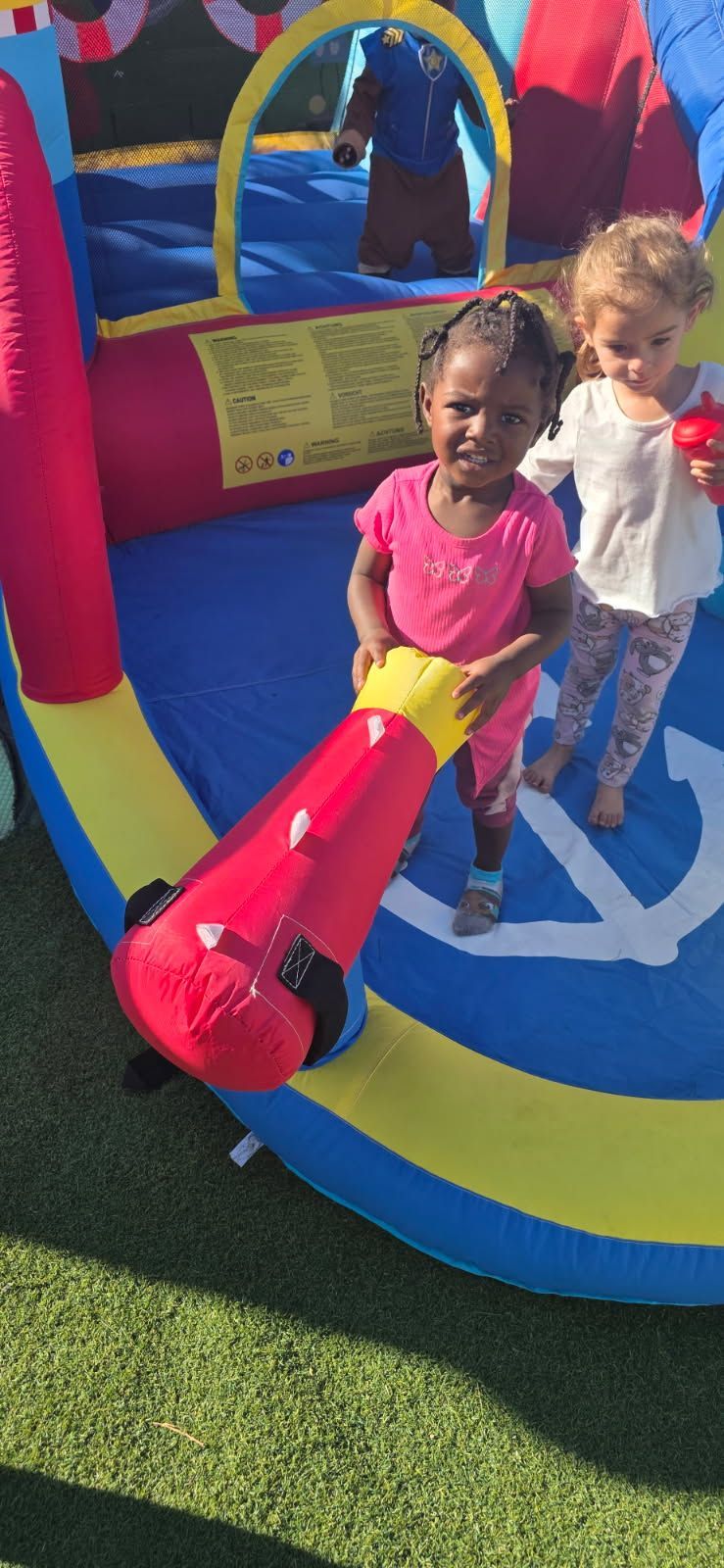 Two children play in a colorful inflatable bounce house. One holds a red cannon.