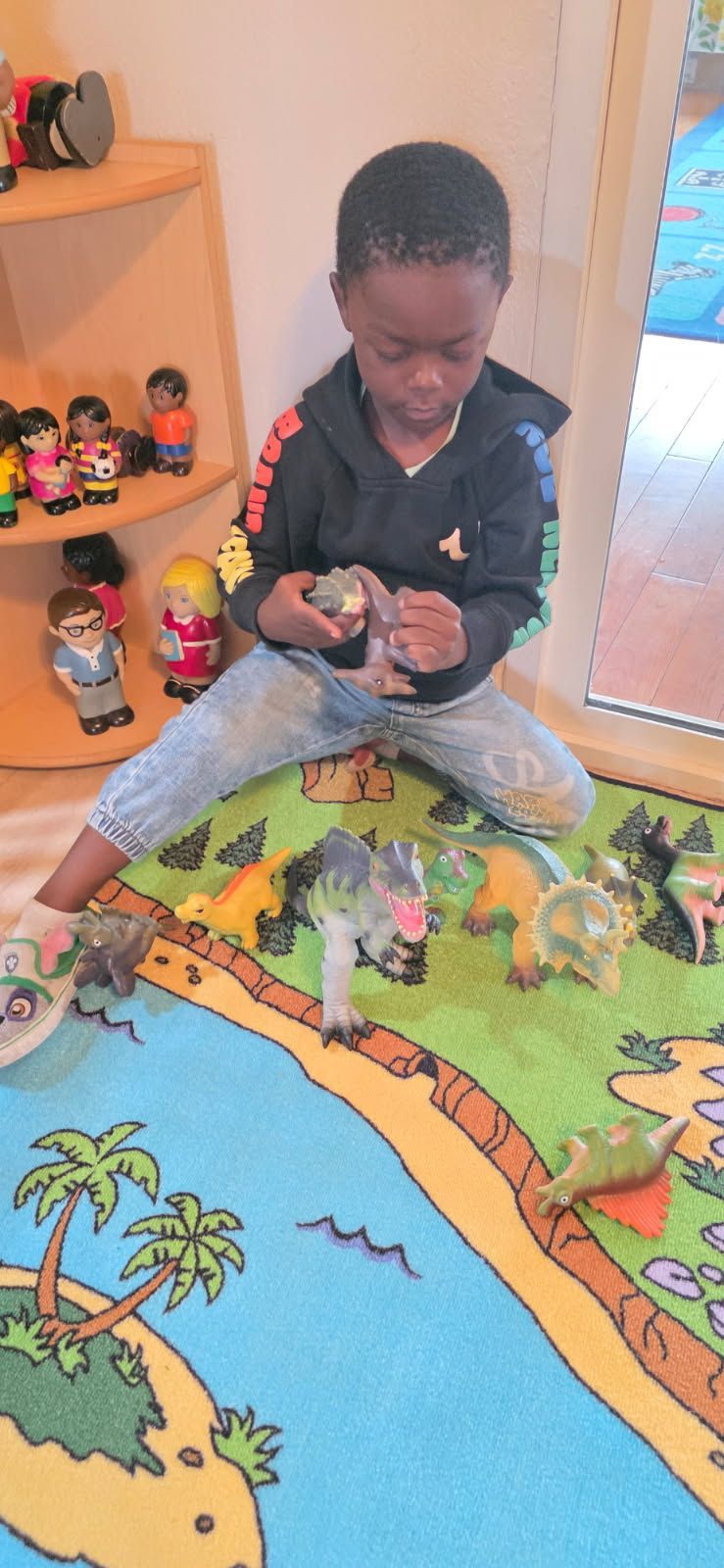 A child sits playing with toy dinosaurs on a colorful rug.