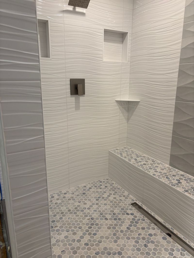 Tiled shower with a bench, built-in shelves, and a patterned floor. White and gray tones.