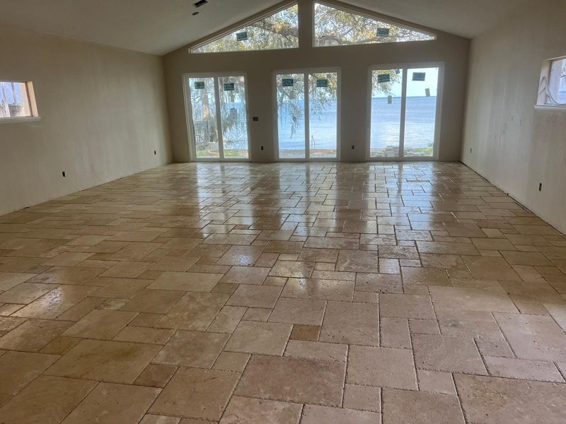 Spacious room with light brown tile floor, large windows overlooking water, and light-colored walls.