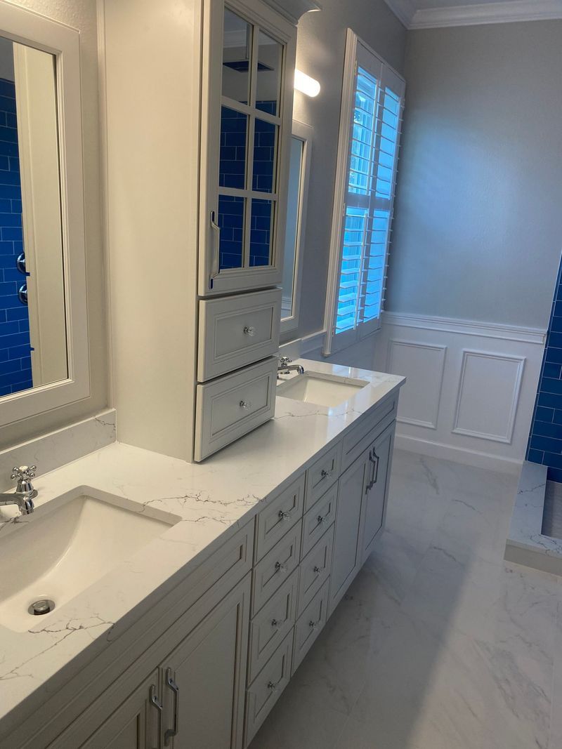 White bathroom with double vanity, cabinetry, large mirror, and window with blue accents.
