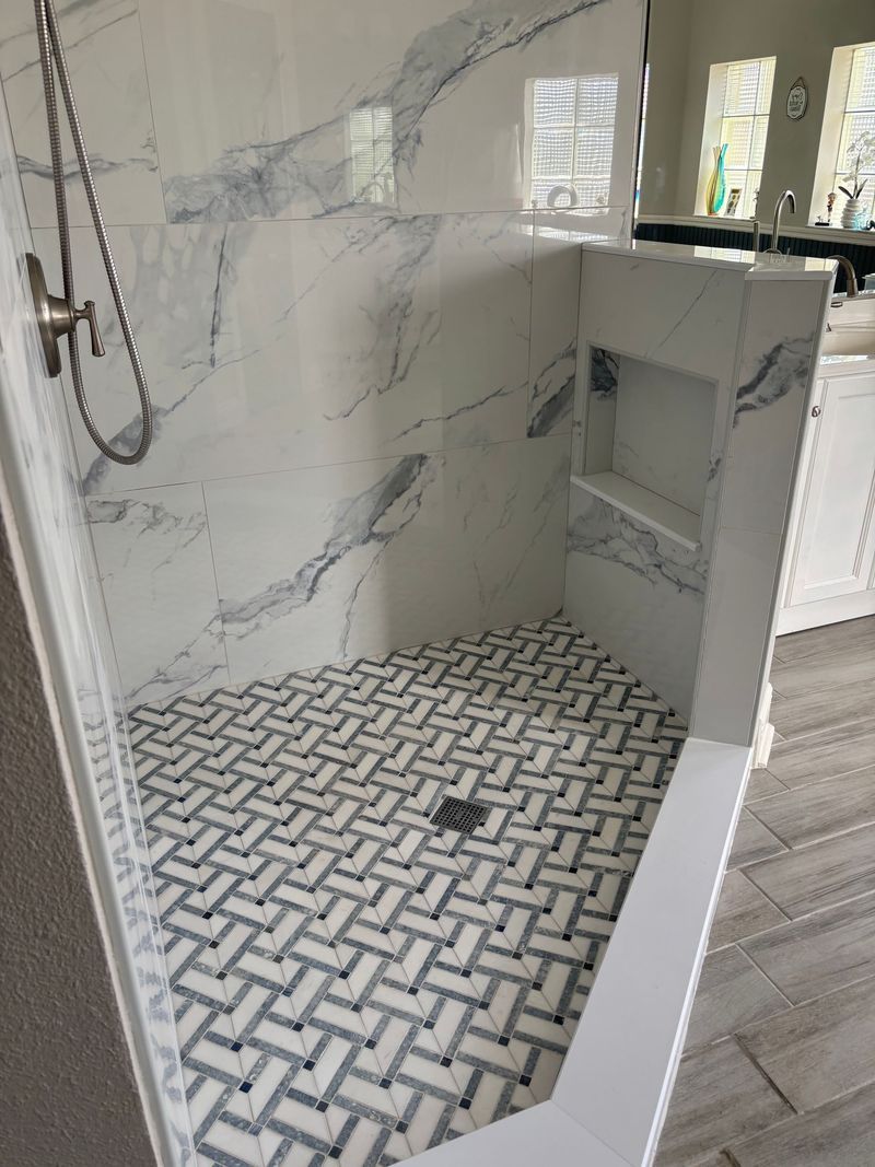 Shower with herringbone tile floor and marble-look walls, with a built-in shelf.