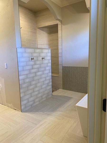Bathroom under construction with tiled shower, light walls, and white freestanding tub.