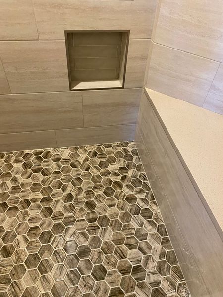 Shower corner with hexagon tile floor, built-in bench, and recessed shelf. Light brown and gray tones.