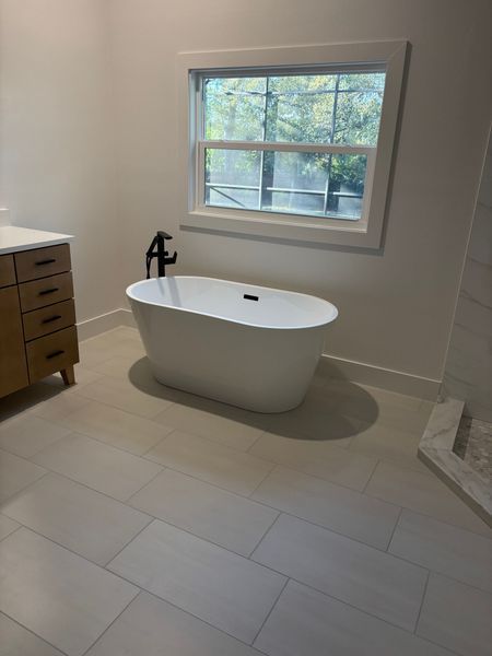 Modern bathroom with a white freestanding bathtub beneath a window.