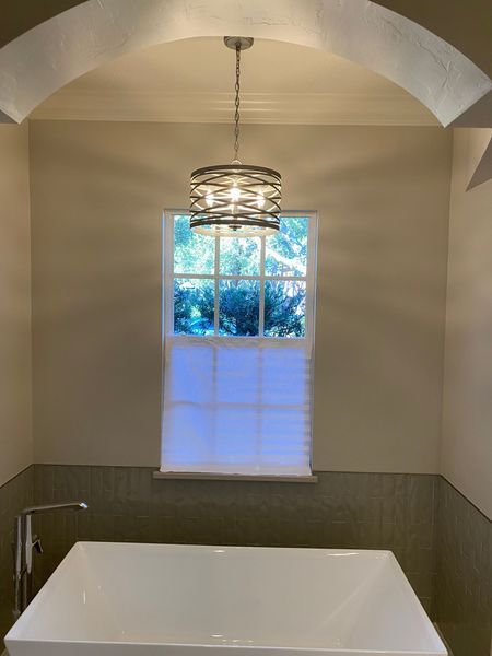 Bathroom with white tub, window, and modern chandelier hanging from an arched ceiling.