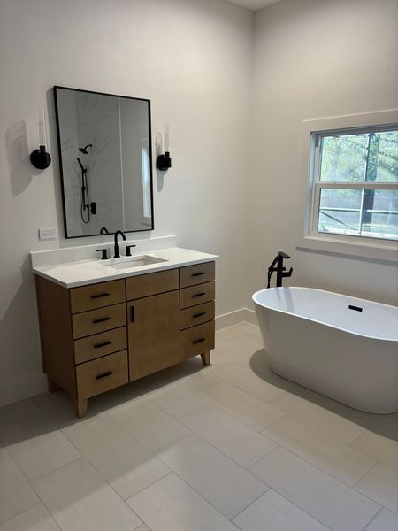 Bathroom with wood vanity, large mirror, soaking tub, and window. Neutral color palette.