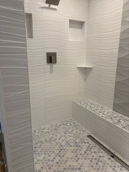 White tiled shower with textured walls, built-in bench, and patterned floor.