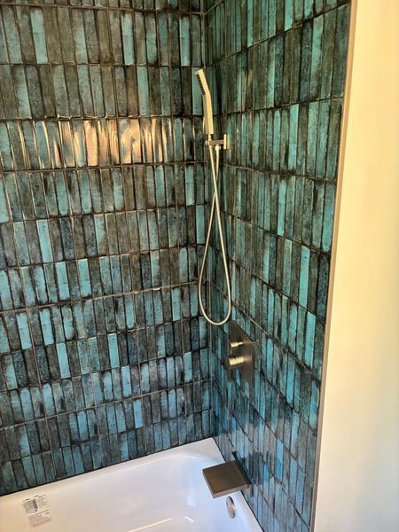Blue and grey patterned tile shower enclosure with a white bathtub. Showerhead and control panel are visible.