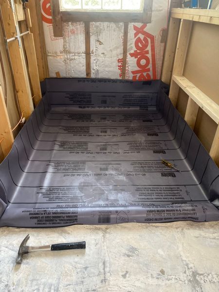 Shower pan liner installed in a framed-out area, with a hammer on the floor.