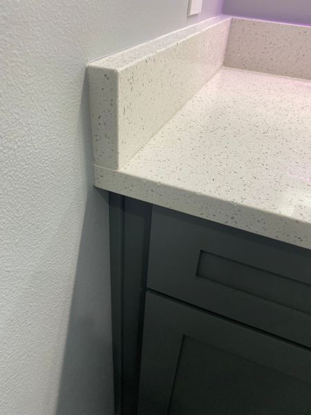White speckled quartz countertop with backsplash on gray cabinet.