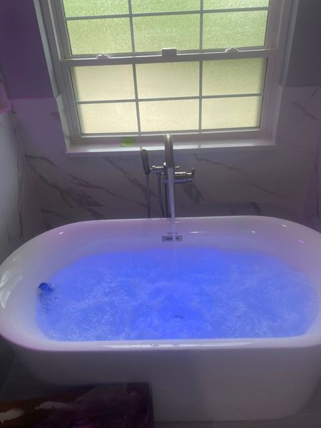 White bathtub filled with blue water under a window.