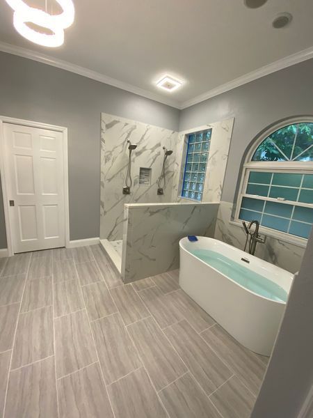 Modern bathroom with marble shower, freestanding tub, and gray tile floor.