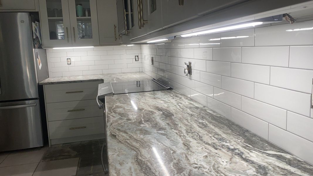 Kitchen remodel with gray countertops, white subway tile backsplash, under-cabinet lighting, and stainless steel appliances.