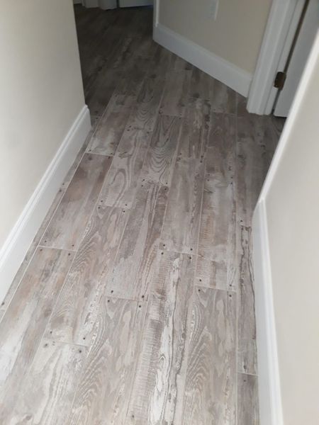 Narrow hallway with light-colored wood-look flooring. White baseboards and walls. Doorway visible at the end.