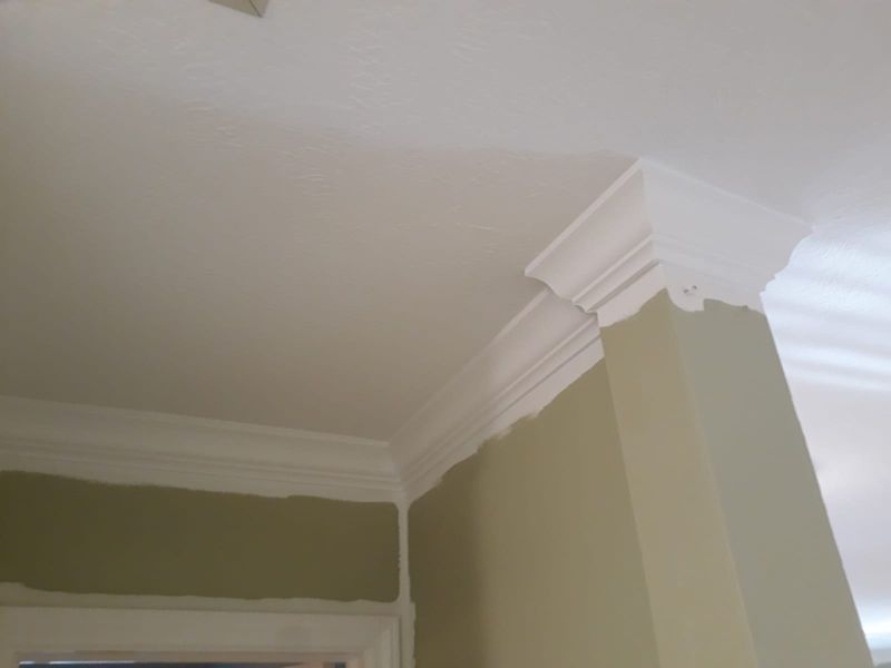 White crown molding installed in the corner of a room with green walls and white ceiling.
