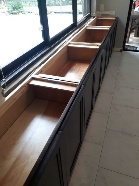 Built-in wooden bench with open storage compartments below a large window. Dark brown cabinet doors, light wood interior.