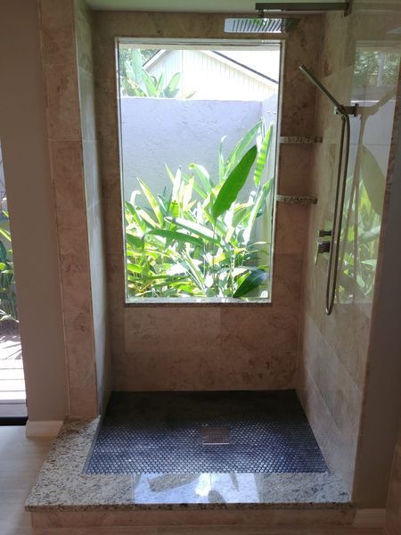 Shower with window looking onto greenery, beige tile walls, dark gray tiled floor, and chrome shower fixtures.