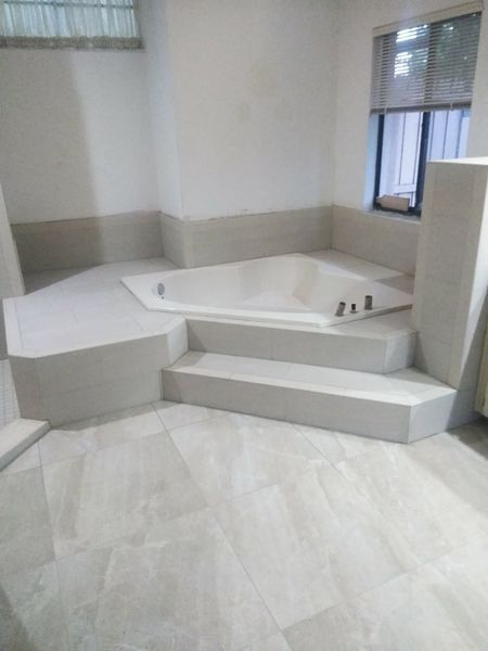 Bathroom with raised platform for a large, white, triangular bathtub; steps lead up to it; beige tile floor.