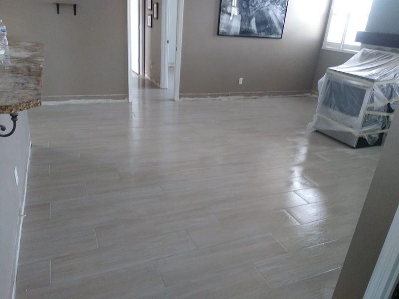 Newly installed light-colored tile flooring in a room, with a stove covered in plastic and neutral-toned walls.