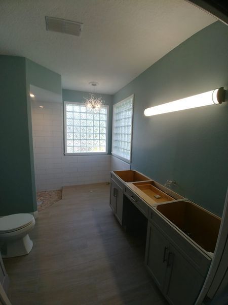 Empty bathroom with pale blue walls, glass block window, and unfinished vanity cabinets.