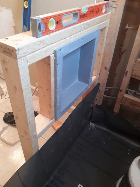 Wooden shower niche being built; level resting on top. Black waterproofing membrane on floor below.