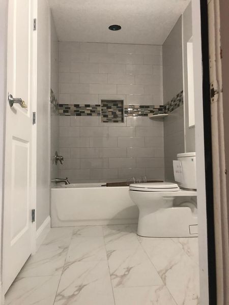 Newly renovated bathroom with white and gray tile, bathtub, and toilet.