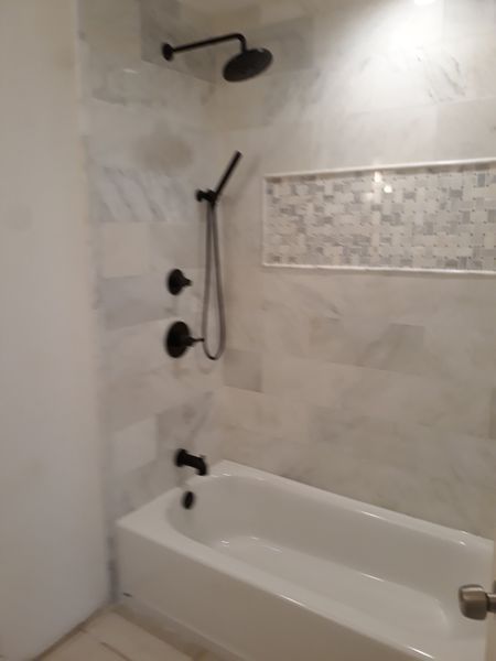 Bathroom with white bathtub, black shower fixtures, and marble-look tiles.